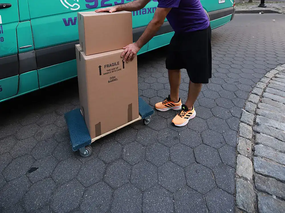 ZeroMax mover wheeling boxes on a dolly beside a moving van for a move from NYC to Las Vegas